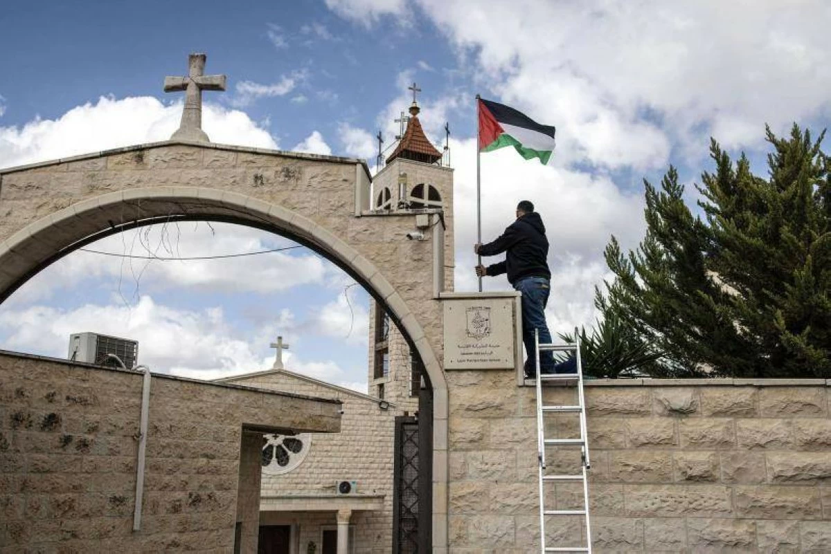A man puts up a Palestinian flag at the entrance of the Our Lady of Visitation Catholic church in the northern West Bank town of Zababdeh on April 10 (AFP photo)