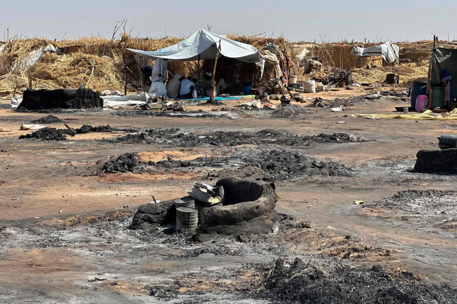 A displaced Sudanese woman who left El Fasher after its fall with others, walks amid the remains of a fire that broke out at a camp in Tawila on February 11 (AFP photo)