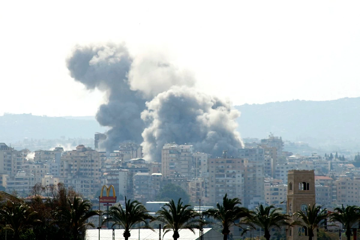 Smoke rises behind palm trees and a McDonald's "Golden Arches" logo from the site of an Israeli airstrike that targeted the Al-Hosh area near the coastal Lebanese city of Tyre on April 14, 2026  (AFP photo)
