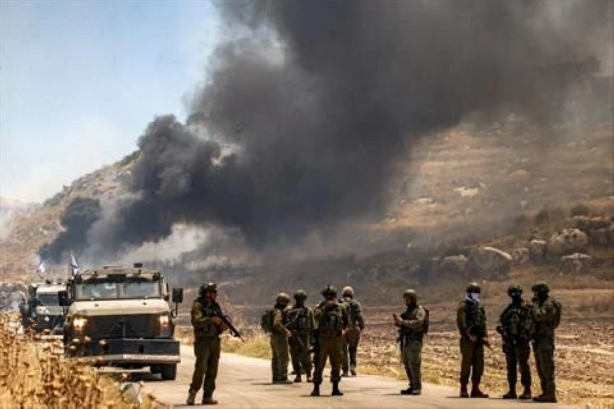 Israeli security forces stand guard along a road while behind smoke billows from an area reportedly set ablaze by Israeli settlers in the Palestinian village of Idna, west of Hebron in the occupied West Bank, on June 5, 2026 (AFP photo)