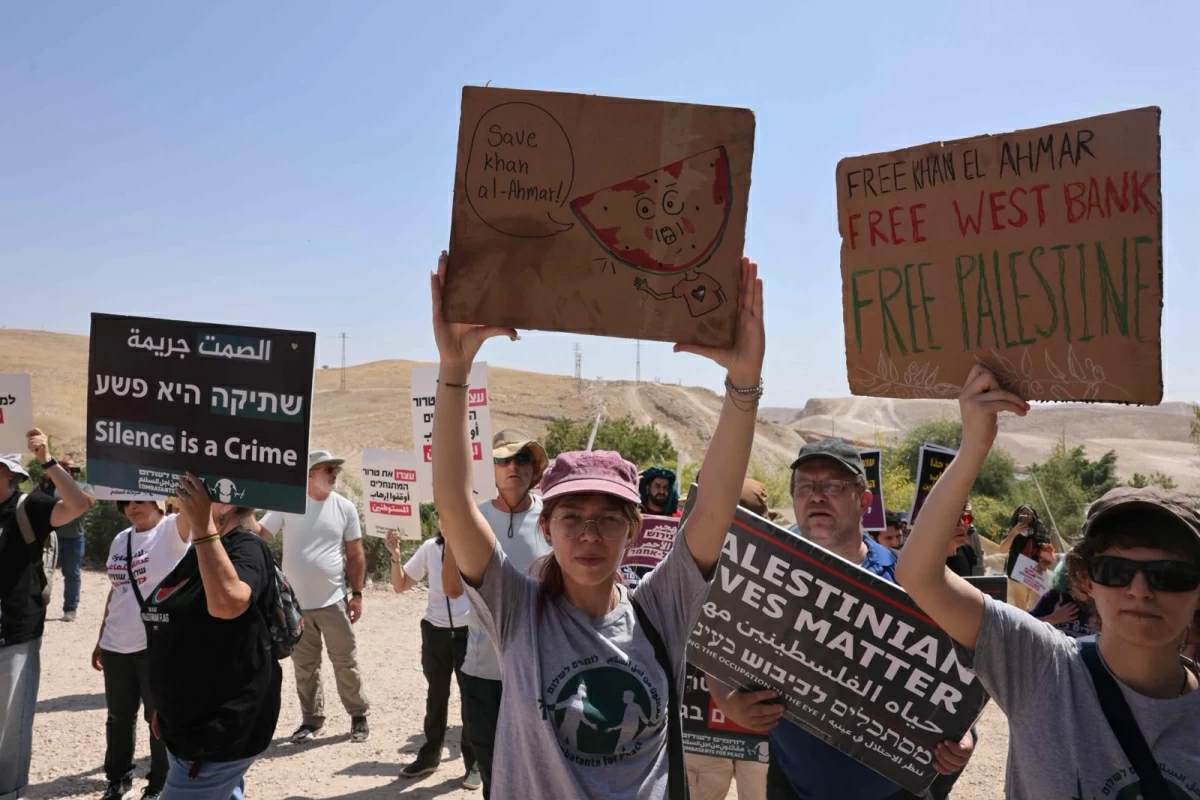 Palestinians and Israeli left-wing activists hold placards during their protest march against the planned eviction of the villagers at Khan al-Ahmar in the Israeli-occupied West Bank on June 12, 2026 (AFP photo)