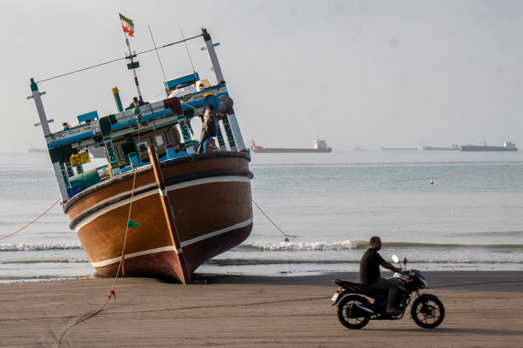 In this picture obtained from Iran's ISNA news agency on April 24, 2026, an Iranian man rides his motorcycle past a boat at Suru Beach in Bandar Abbas along the Strait of Hormuz (AFP photo)