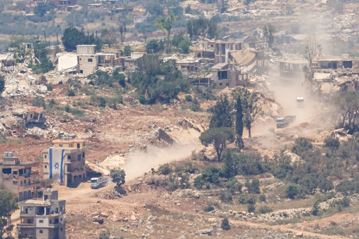 This picture taken from a position in the Upper Galilee in northern Israel, shows an Israeli construction truck passing an Israeli flag covering part of a destroyed building in the southern Lebanese village of Taybeh near the border on June 18, 2026 (AFP photo)