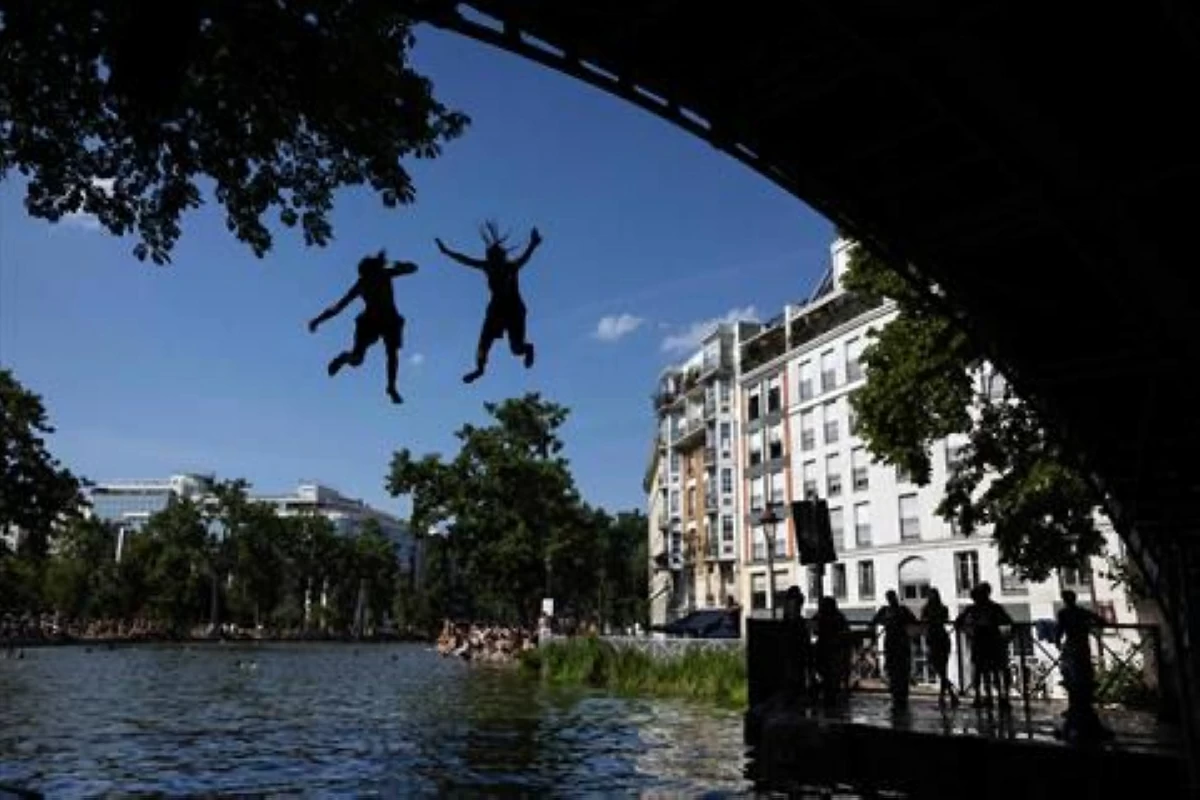 Young people jump from a bridge into the Canal Saint-Martin during a heatwave in Paris on June 22, 2026 (AFP photo)