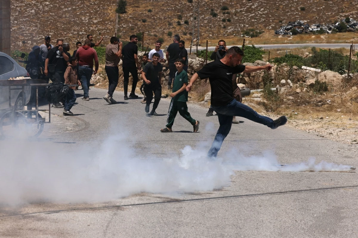 A Palestinian kicks away a teargas cyclinder fired by Israeli forces guarding bulldozers demolishing the home and shops belonging to the Al Atrash family, just south of the Israeli-occupied West Bank city of Hebron on June 23 (AFP photo)