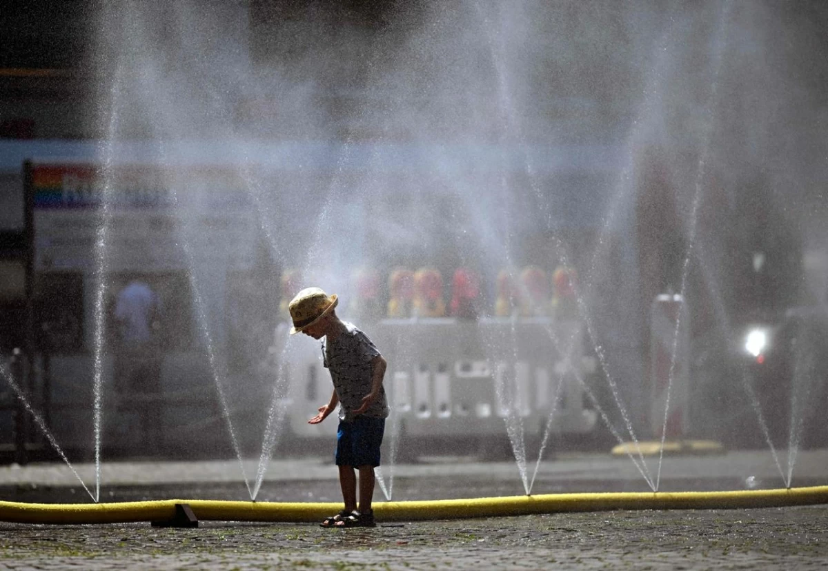A young boy stands next to water hoses spilling water to provide relief from the summer heat as part of Cologne’s climate adaptation measures in Cologne, western Germany on June 25, 2026 during a heatwave in Europe (AFP photo)