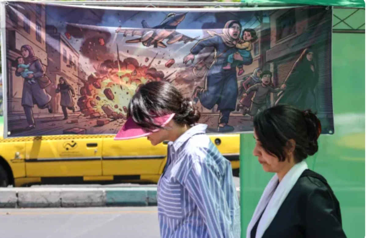 Women walk past a banner depicting the US-Israel attacks on Iran in the capital, Tehran, on May 9, 2026 (AFP photo)