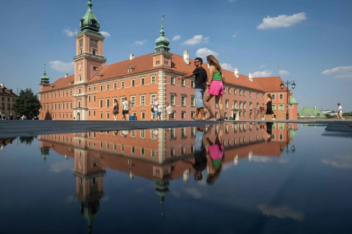 People walk past the Royal Castle reflected in the pond on Warsaw's Old Town as thermometers show record temperatures during a heatwave that has reached Poland on Sunday (AFP photo)