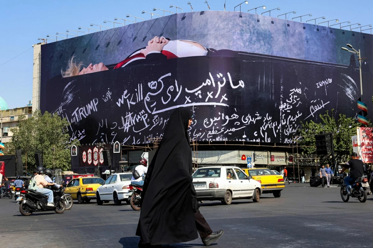 A woman crosses Tehran's Enghelab Square on July 15, 2026, past a giant anti-US billboard featuring US president Donald Trump in a coffin with text in Persian reading 