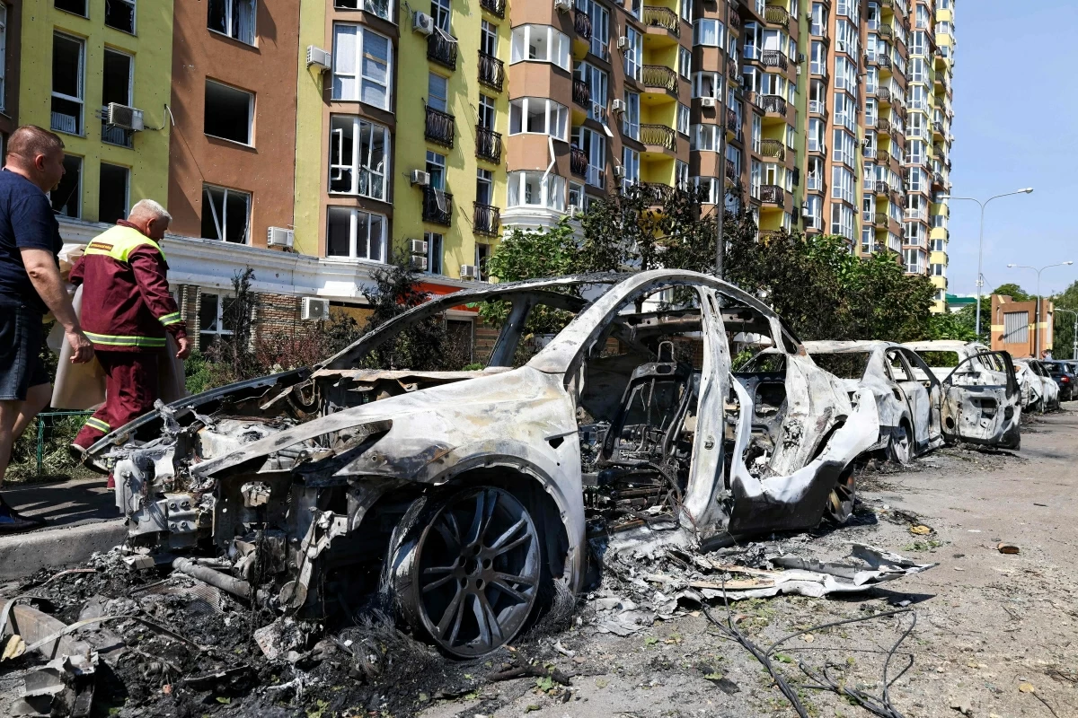 People walk past damaged cars parked in a street following missile strikes in Kyiv on Sunday (AFP photo)