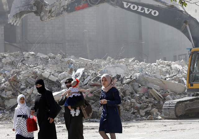 A Syrian family walks by the rubble of destroyed buildings being removed by a bulldozer in Harasta, on the outskirt of the Syrian capital Damascus, on Wednesday. After a blistering weeks-long assault, Syria's government recaptured the town of Harasta in March, and displaced families have been trickling back to check if their homes survived (AFP photo)