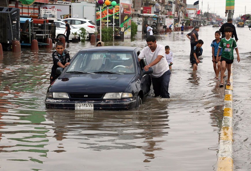 Iraqis push a car, submerged in water, as others make their way through a flooded street after heavy rain fell in Baghdad on Thursday (AP photo)