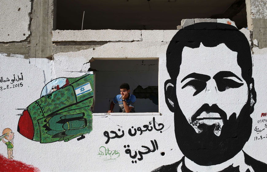 A Palestinian youth stands behind a wall sprayed with graffiti depicting 31-year-old Mohammed Allan, a Palestinian held by Israel without trial and who has reportedly slipped into a coma after a nearly two-month hunger strike, on Sunday, in Gaza City (AFP photo)