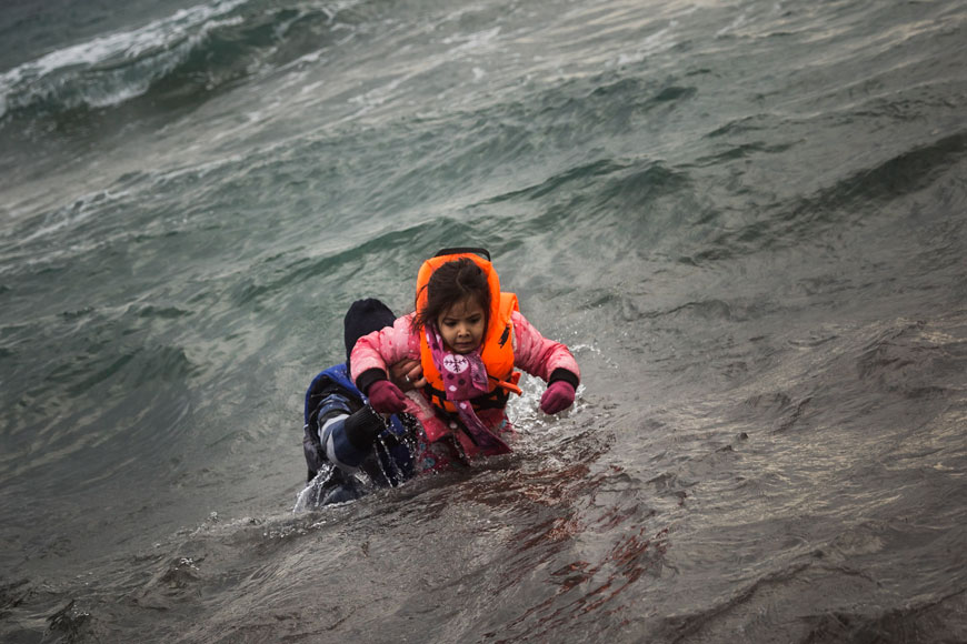A man carries a child as they try to reach a shore after falling into the sea while disembarking from a dinghy on which they crossed a part of the Aegean Sea with other refugees and migrants, from Turkey to the Greek island of Lesbos, on Sunday (AP photo)