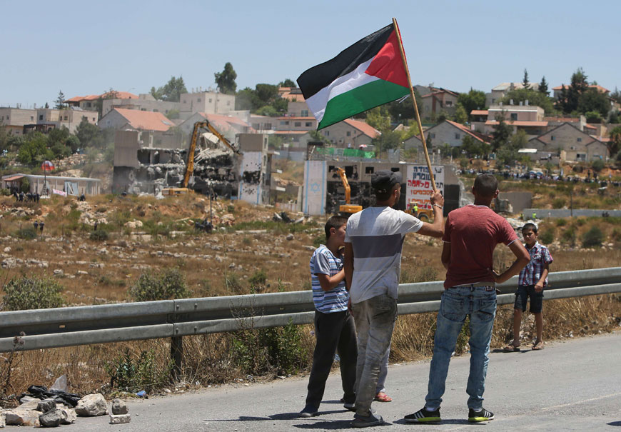 Palestinians from the Jalazoun refugee camp hold their national flag as they watch at bulldozers demolishing the so-called Dreinoff buildings under an Israeli high court ruling in the settlement of Beit El, north of Ramallah in the occupied West Bank, on Wednesday (AFP photo)