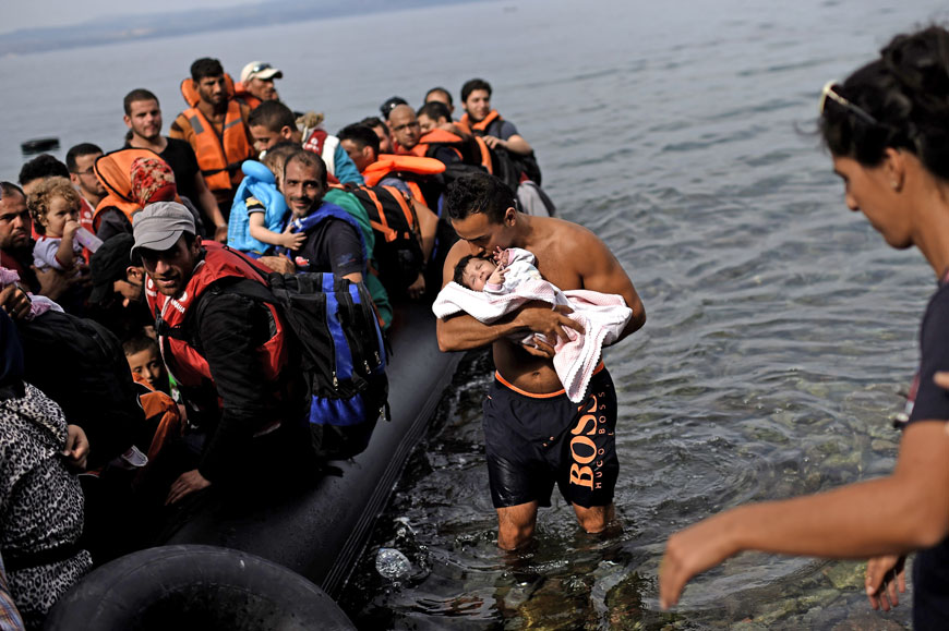 A man kisses a baby as he helps refugees and migrants arriving on an inflatable dinghy to the Greek island of Lesbos after crossing the Aegean sea from Turkey on Saturday (AFP photo)