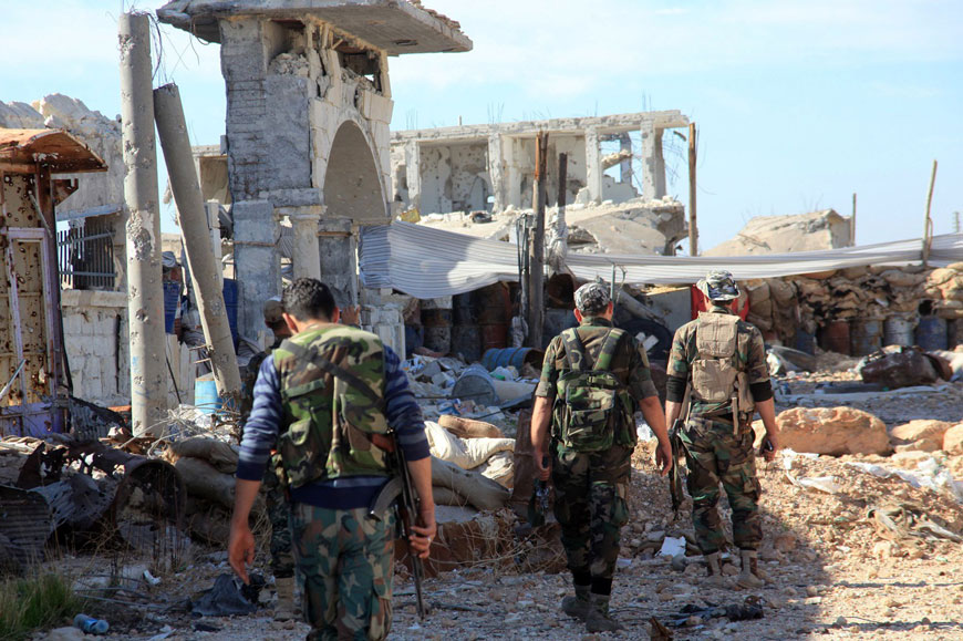 Pro-government fighters walk past debris in the Syrian town of Arbid on the outskirts of the Kweyris military air base, in the northern Syrian province of Aleppo, on Thursday (AFP photo)