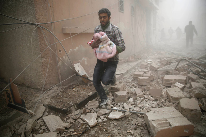 A Syrian man carries a baby wrapped in a blanket following air strikes on the town of Douma in the Eastern Ghouta region, a rebel stronghold east of the capital Damascus, on Sunday (AFP photo)