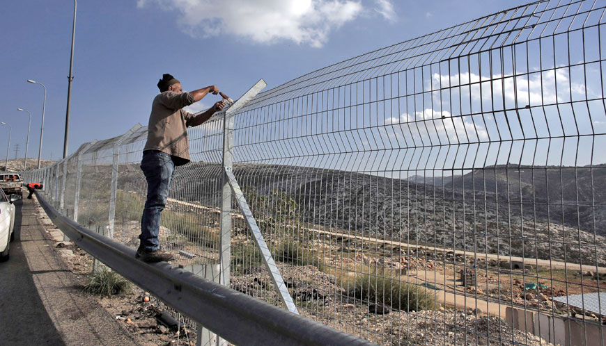 Workers add barbed wire to part of Israel’s controversial separation barrier along Highway 443, which runs from the outskirts of Tel Aviv to the northern entrance of Jerusalem with a 20-kilometre stretch through the West Bank, on Sunday (AFP photo)