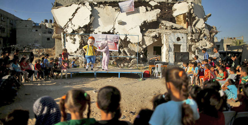Palestinians wearing costumes perform to amuse children in front of a house, that witnesses said was destroyed by Israeli shelling during a 50-day war last summer, in the east of Gaza City on Wednesday.  The majority of children living in Gaza’s hardest-hit areas during last year’s conflict are showing signs of severe emotional distress and trauma, including frequent bed-wetting and nightmares, a global children’s charity said on Monday (Reuters photo by Mohammed Salem)