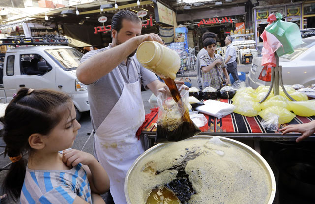 A Syrian vendor pours a bag of traditional liquorice juice for a young girl in Damascus’ Midan neighbourhood, which is renowned for its sweet delicacies, as people shop prior to breaking their fast during the holy month of Ramadan on Tuesday (AFP photo)