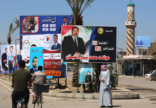 Two Iraqi men ride their bikes past posters of candidates for legislative elections in Ramadi, Anbar province, western Iraq, on Tuesday (AFP photo)