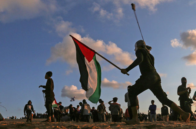 A Palestinian protester carries a national flag as he hurls stones during a demonstration calling for an end to the Israeli blockade on Gaza, on a beach in Beit Lahia near the maritime border with Israel, on Monday (AFP photo)