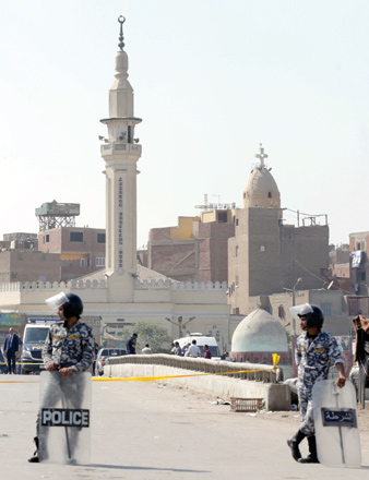 Egyptian police officers stand guard as others inspect the body of the attacker outside a church in Qalyubiyah, north of Cairo, on Saturday. Police said it killed six suspected terrorists, on Monday   (Reuters photo)