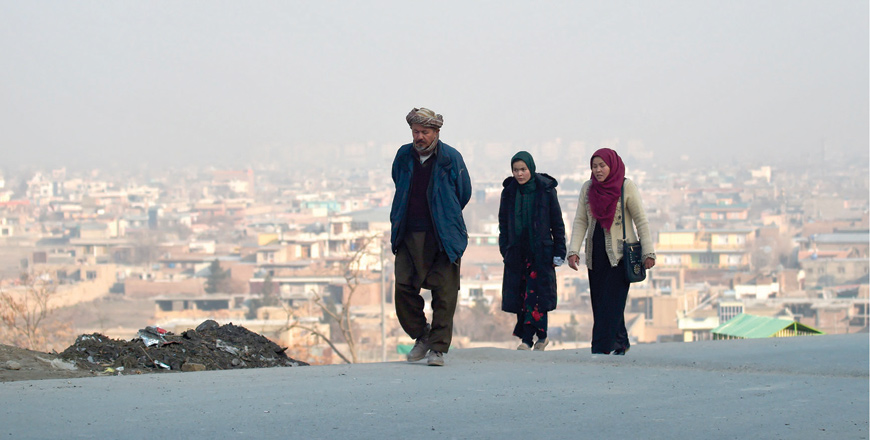A man walks along with women on a hillside overlooking Kabul, on Saturday (AFP photo)