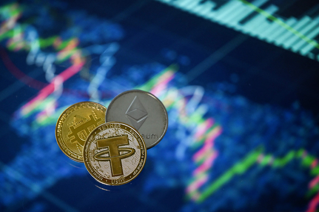 This illustration photo taken in London on Sunday shows gold plated souvenir cryptocurrency Tether (USDT), Bitcoin and Etherium coins arranged beside a screen displaying a trading chart (AFP photo)