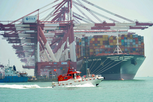 A boat sails past as a cargo ship berths at a port in Qingdao, in China's eastern Shandong province, on Monday (AFP photo)