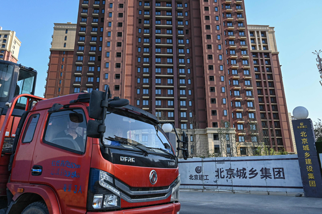 Truck drivers drive past a housing complex under construction in Beijing on Friday (AFP photo)