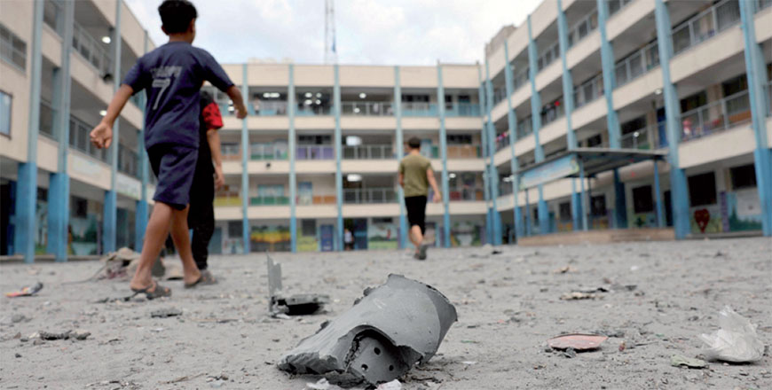 Palestinian children walks past debris in the courtyard of a school run by UNRWA following Israeli airstrikes targeting Gaza City on Monday  (AFP photo by Mohammed Abed)