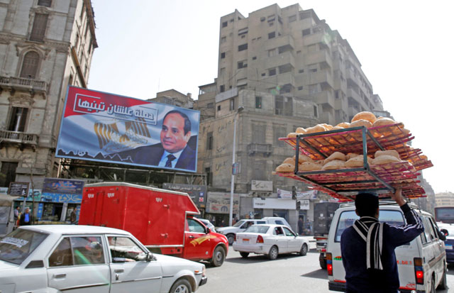 A man rides a bicycle as he carries breads on his head along a busy street near a poster of Egypt's President Abdel Fattah Al Sisi from the campaign titled Alashan Tabneeha in Arabic , which means (So You Can Build It), for the upcoming presidential election in Cairo, Egypt, on Monday (Reuters photo)