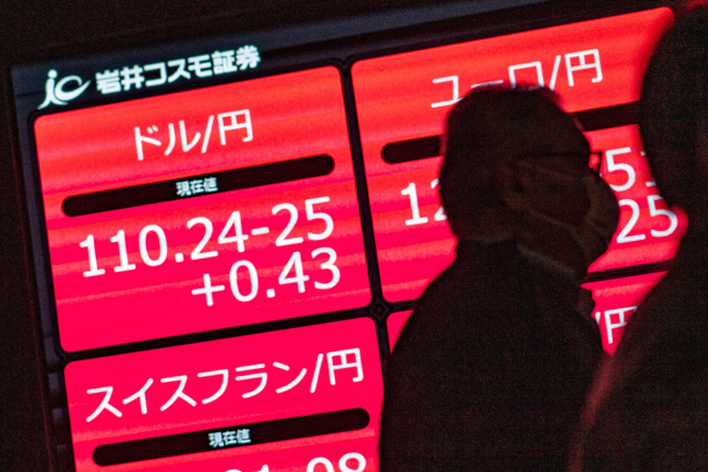 People walk past an electronic quotation board displaying the Japanese yen's exchange rate against the US dollar (top left ) after it broke the 110 yen mark for the first time since March 2020, at the Tokyo Stock Exchange in Tokyo, on Tuesday (AFP photo)