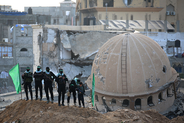 Palestinian Hamas militants gather today at the site of the handover of the bodies of four Israeli hostages in Khan Yunis in the southern Gaza next to a mosque destroyed in Israeli bombardment during the war (AFP photo)