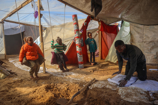 Palestinian father Tayseer Obaid who was displaced with his family from the north of the besieged Gaza Strip, prepares to dig a trench in his tent in an attempt to protect his children from the cold and Israeli strikes (AFP photo)