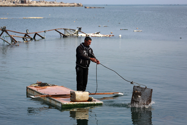 A Palestinian man stands on the door of a refrigerator that he uses as a makeshift rowing boat, as he throws his fishing basket into the sea at the port of Gaza City yesterday (AFP photo)