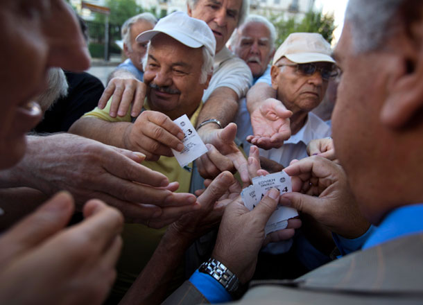 A bank employee distributes tags with queue positions to pensioners as they wait outside the main gate of the national bank of Greece to withdraw a maximum of 120 euros ($134) in central Athens on Thursday (AP photo)