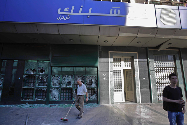 A man sweeps glass off the ground along a street outside the local branch of a Lebanese bank after it was vandalised by protesters earlier, in Al Nour Square in Lebanon's northern port city of Tripoli, on Friday  (AFP photo)
