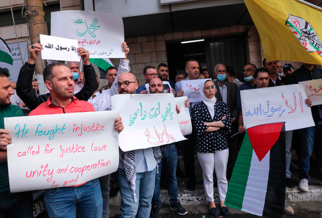 Palestinians lift placards during a rally in front of the municipality of the West Bank city of Hebron, in response to comments by French President Emmanuel Macron defending cartoons of Prophet Mohammed, on Sunday (AFP photo)