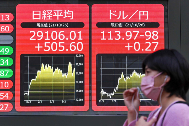 A pedestrian walks past an electronic quotation board displaying the closing share prices of the Tokyo Stock Exchange (left) and the yen rate against US dollar (right) in Tokyo on Tuesday (AFP photo)