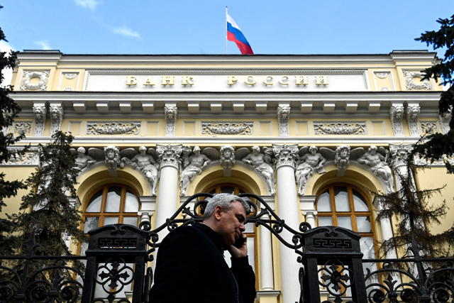 A man on the phone walks past the Russian Central Bank headquarters as the Russian flag flies, in downtown Moscow, on Friday (AFP photo)