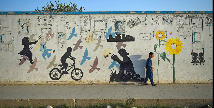 In this photo taken on Sunday, a boy walks alongside a wall covered with street art in Mazar-e-Sharif  (AFP photo)