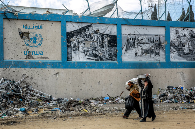 People walk past UNRWA’s damaged Gaza City headquarters on February 15, 2024 (AFP Photo)  
