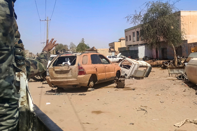 A Sudanese army soldier gestures from the back of a vehicle as it drives past damaged cars lying along a street in Khartoum yesterday (AFP photo)