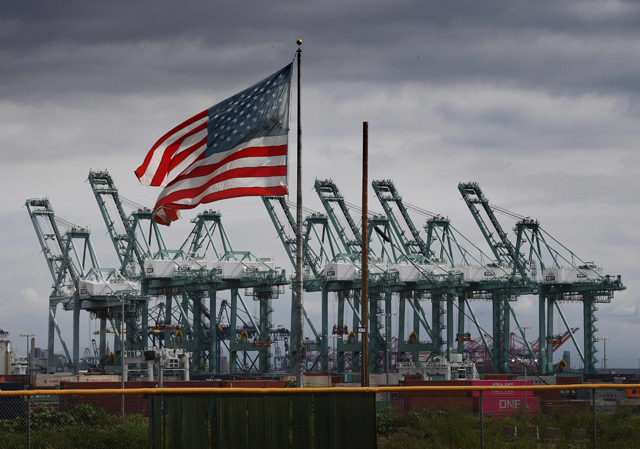 In this photo taken on Monday, the US flag flies over shipping cranes and containers in Long Beach, California (AFP file photo)  