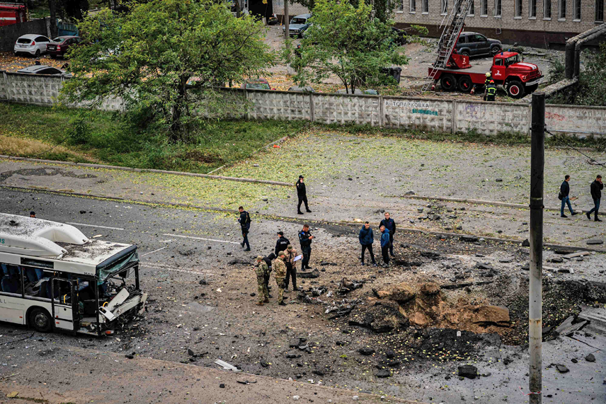 Investigators examine a crater next to a damaged bus, following a missile strike in Dnipro on Monday (AFP photo)