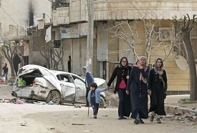People walk near a damaged car in Afrin, Syria, on Thursday (Reuters photo)