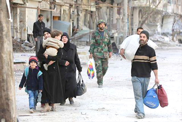 Syrian people walk down a street past a destroyed building on Sunday, as civilians and rebels prepare to evacuate the town of Ain Tarma in the Eastern Ghouta region on the outskirts of the capital Damascus (AFP photo)